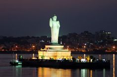 the statue of liberty is lit up at night with lights reflecting in the water and buildings behind it