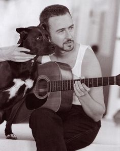 a man holding a guitar while sitting next to a dog