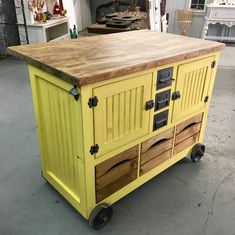 a yellow kitchen island with drawers on wheels in a room filled with furniture and other items