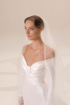 a woman in a white wedding dress with a veil on her head and shoulder, looking off to the side