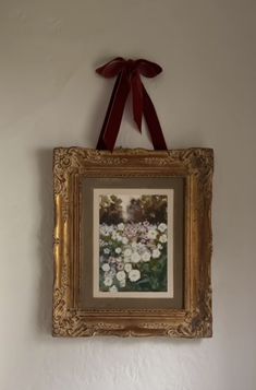 a painting hanging on the wall with a red bow around it's neck and an empty frame