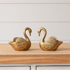 two gold swan figurines sitting on top of a wooden table