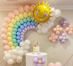 there is a cake and balloons on the table in front of this rainbow themed wall