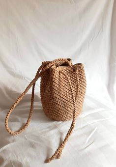 a small woven bag sitting on top of a white cloth covered tablecloth with a knoted handle