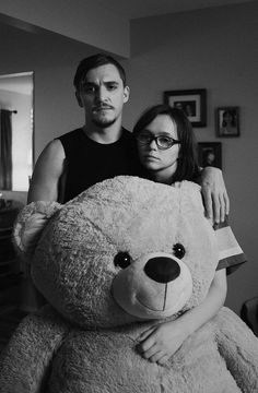 a man standing next to a woman holding a large teddy bear in front of her