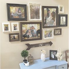 a bunch of pictures hanging on the wall next to a table with vases and flowers