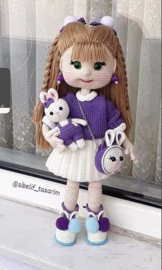 a doll with long hair holding two small stuffed animals in front of a window sill