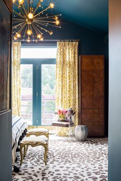 a bedroom with a chandelier and yellow curtains on the window sill, next to a bed