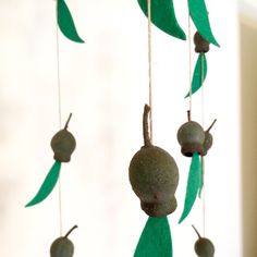 a mobile with green leaves and fruit hanging from it's sides in front of a window