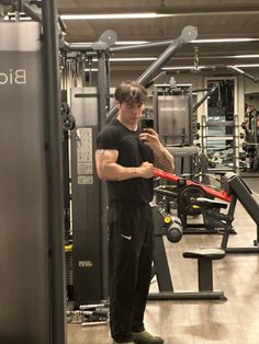 a man standing in front of a gym machine holding a cell phone to his ear