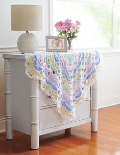 a crocheted baby blanket on a dresser next to a vase with flowers in it