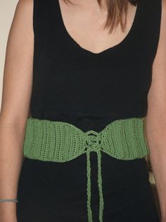 a woman wearing a black top with a green belt around her waist and the bottom part of her body