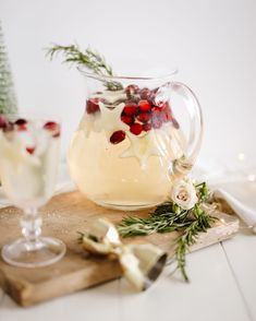 a glass pitcher filled with white wine and garnished with red berries sits on a cutting board