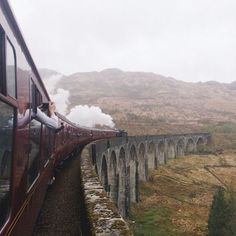 a train traveling over a bridge with steam pouring out of it's chimneys