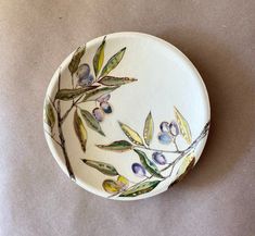 a white bowl with an olive branch painted on the side and purple berries in the middle