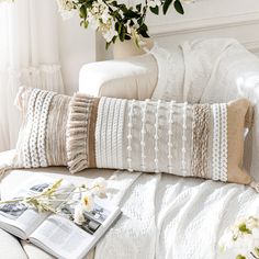 a white couch sitting next to a book on top of a table with flowers in it