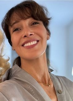 a woman smiling and wearing a silver jacket