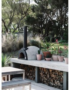 a stone oven sitting on top of a cement bench surrounded by potted plants and trees