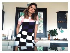 a woman standing in a kitchen next to a counter with a black and white checkered dress on