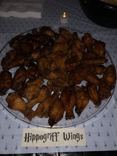 a plate full of chicken wings sitting on a table with a candle in the background