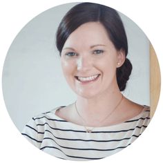 a woman smiling in front of a white background with a wooden sticker around her neck