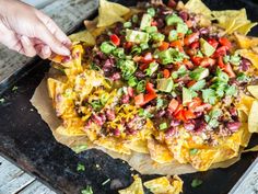 someone is dipping tortilla sauce on top of the nachos with toppings