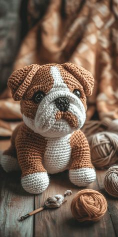 a crocheted bulldog sitting on top of a wooden floor next to balls of yarn