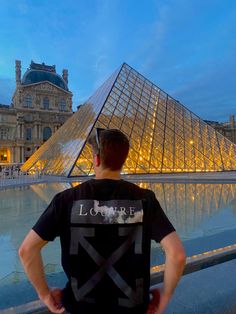 a man standing in front of a large pyramid at night with his back to the camera