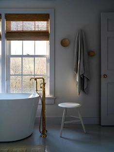 a white bath tub sitting under a window next to a stool and table with a towel on it