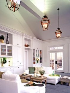 a living room filled with white furniture and lots of lights hanging from the ceiling above