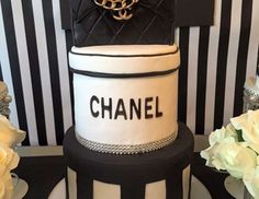 a black and white cake with chanel on it's tiered tower, surrounded by flowers