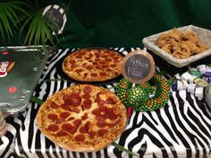 two pizzas sitting on top of a zebra print table cloth next to other food