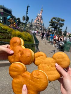 two people holding up mickey mouse cookies in front of the disneyland world park entrance area