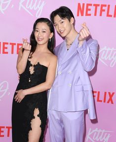 two people standing next to each other in front of a pink wall and posing for the camera