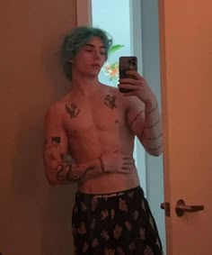 a man with green hair and tattoos taking a selfie in front of a mirror