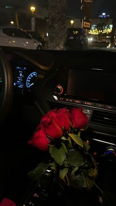 a red rose sitting in the center console of a car at night with city lights behind it