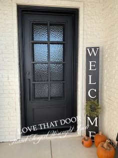 a black front door on a white brick building with pumpkins and a welcome sign