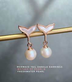 Mermaid Tail Dangle Earrings lovingly designed by Love Estella Jewelry The mermaid tail is adorned with a shimmering natural Mother-Of-Pearl that adds a touch of elegance and sophistication to the design. To give the earrings an extra touch of charm, we have a natural Freshwater Pearl dangling gracefully from the mermaid tail, making them the perfect accessory for any occasion. Made in 925 silver plated with a thick layer of 18K Gold. Choose from three hardware - Rose Gold, Silver or Yellow Gold Mermaid Tail Jewelry, Ocean-inspired Shell-shaped Pearl Earrings, Ocean-inspired Gold Shell Earrings, Ocean-inspired Shell Dangle Earrings, Mermaid Tail Earrings, Black Spinel Bracelet, Summer Promotion, Silver Mermaid, Freshwater Pearl Earrings