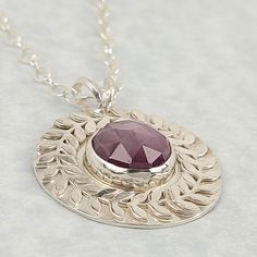 Shimmering in quiet lyrical elegance, a circle of laurel leaves form a never-ending wreath that surrounds a stunning rose cut stone in this purple sapphire necklace. Hand-wrought from recycled sterling silver, a round pendant is set with a unique pinkish-purple rose-cut sapphire that is bordered by a continuous circle of laurel leaves. Sapphire pendant suspends freely from an 18-inch sterling silver cable chain. Laurel leaves have denoted glory and achievement dating as far back as Roman times, Laurel Leaf, Pinkish Purple, Laurel Leaves, Purple Sapphire, Leaf Wreath, Sapphire Pendant, Purple Rose, Sapphire Necklace, Purple Roses