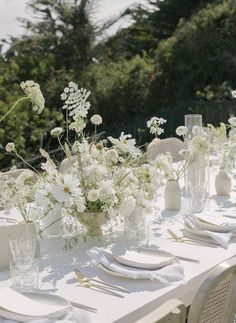 the table is set with white flowers in vases and place settings for dinner guests