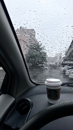 a cup of coffee is sitting on the dashboard of a car in the rain,