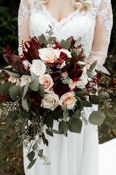 a bridal holding a bouquet of red and white flowers with greenery on it