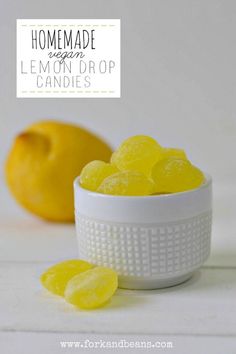 a white bowl filled with lemon drop candies next to a yellow lemon on a white table