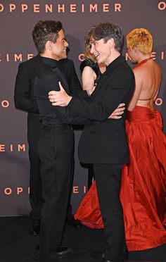 two people hugging each other in front of a red carpet and black wall with words written on it