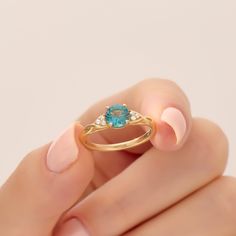 a woman's hand holding a gold ring with an oval blue topaz stone