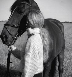 a black and white photo of a woman standing next to a horse in a field