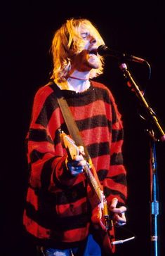 a man standing in front of a microphone while holding a guitar