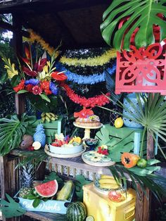 an assortment of fruits and vegetables are displayed on a table in front of a hut