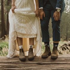 two people standing next to each other on a wooden platform in the woods wearing boots