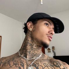 a man with tattoos on his chest wearing a black baseball cap and silver chain necklace